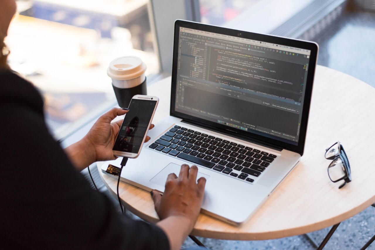 The iowa caucuses – the importance of quality assurance in app development 2 Person looking at phone and at macbook pro